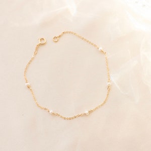 May include: A delicate gold chain bracelet with small white pearls. The bracelet has a simple design and is perfect for everyday wear.