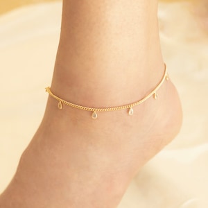 May include: A gold anklet with a delicate chain and small teardrop-shaped charms with clear stones.