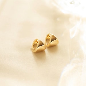 May include: A pair of gold hoop earrings with a unique curved shape. The earrings are simple and elegant, making them a versatile accessory for any occasion.