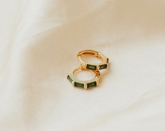May include: A pair of gold hoop earrings with green emerald-like stones set in the hoops.