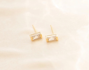 May include: A pair of gold stud earrings with clear rectangular stones.