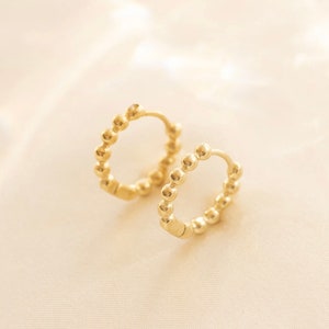 May include: A pair of gold hoop earrings with a beaded design. The earrings are made of small, round beads that are connected together to form a continuous circle.