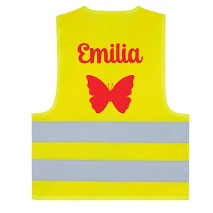 May include: A bright yellow safety vest with reflective stripes. The vest features the name "Emilia" in red script above a red butterfly graphic. The vest is designed for visibility and safety.