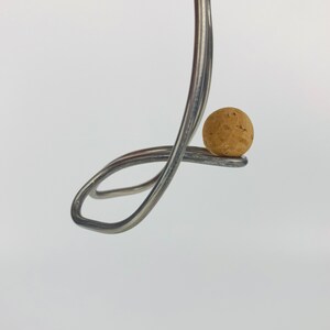 May include: A silver fork bent into a loop, holding a round cork in place.