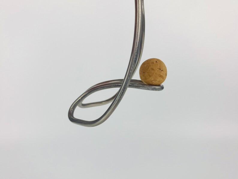 May include: A silver fork bent into a loop, holding a round cork in place.