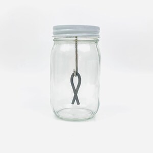 May include: A clear glass jar with a white lid and a metal figure eight hanging inside.