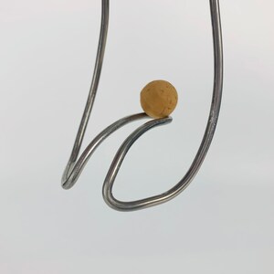 May include: A close-up of a metal sculpture with a brown ball balanced on top. The sculpture is made of two pieces of metal that are bent into a curved shape.