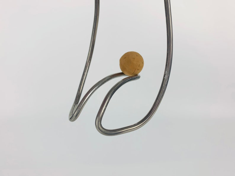 May include: A close-up of a metal sculpture with a brown ball balanced on top. The sculpture is made of two pieces of metal that are bent into a curved shape.