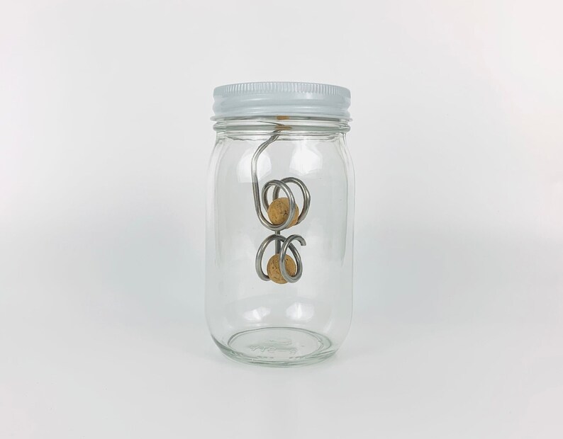 May include: A clear glass jar with a white lid containing two cork balls attached to a metal wire.
