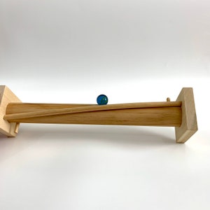 May include: A wooden marble run with a blue marble rolling down the track. The track is made of two wooden pieces that are joined together to form a ramp.
