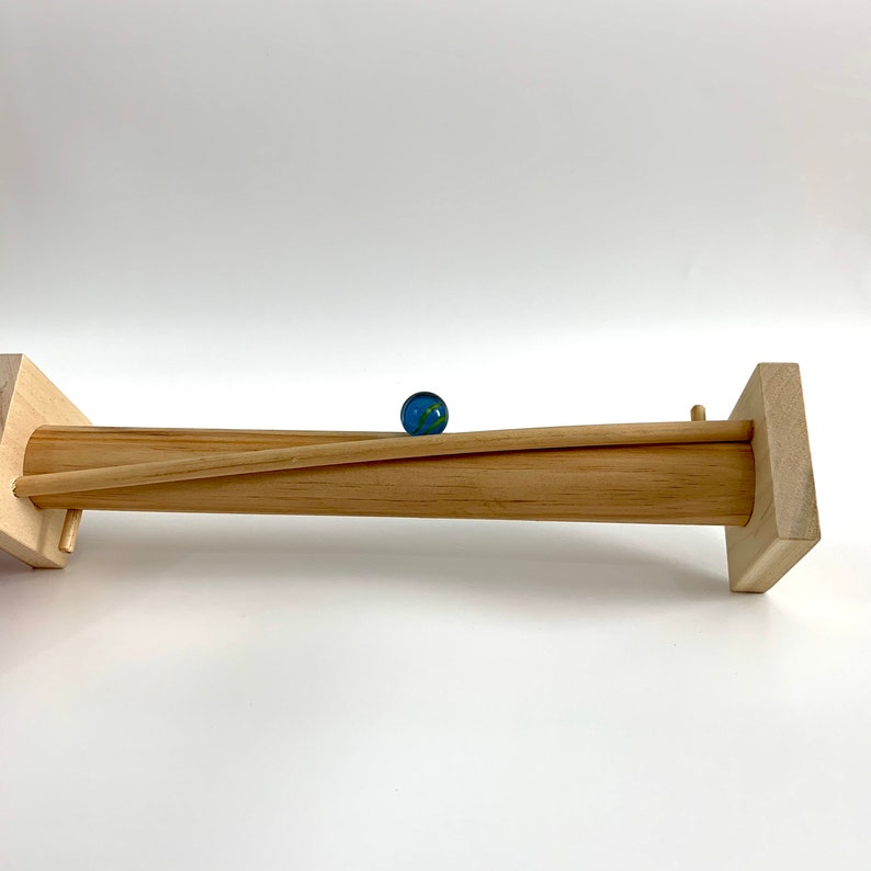 May include: A wooden marble run with a blue marble rolling down the track. The track is made of two wooden pieces that are joined together to form a ramp.