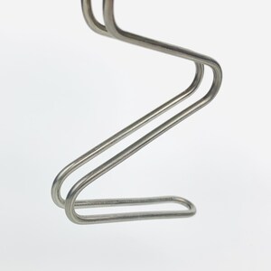 May include: A silver metal coat hanger with a unique, curved design. The hanger is made of two pieces of metal that are joined together to form a Z shape.