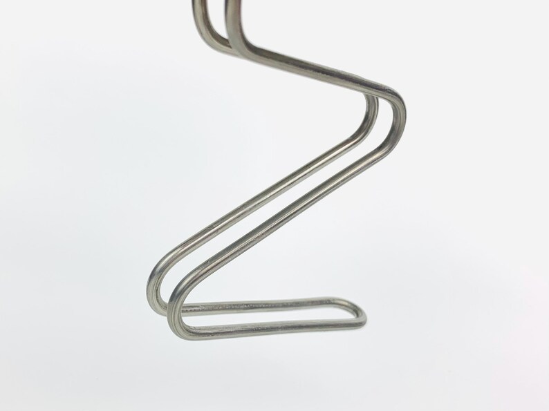 May include: A silver metal coat hanger with a unique, curved design. The hanger is made of two pieces of metal that are joined together to form a Z shape.