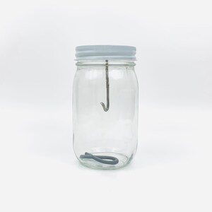May include: A clear glass jar with a white lid and a metal hook inside. A gray rubber band is at the bottom of the jar.