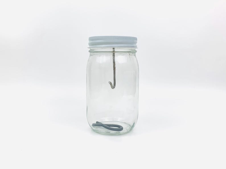 May include: A clear glass jar with a white lid and a metal hook inside. A gray rubber band is at the bottom of the jar.