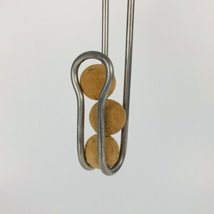 Pu&ograve; includere: Tre sfere di sughero sono sospese da un gancio di metallo. Le sfere sono impilate verticalmente e sono tenute in posizione da un anello di metallo curvo.