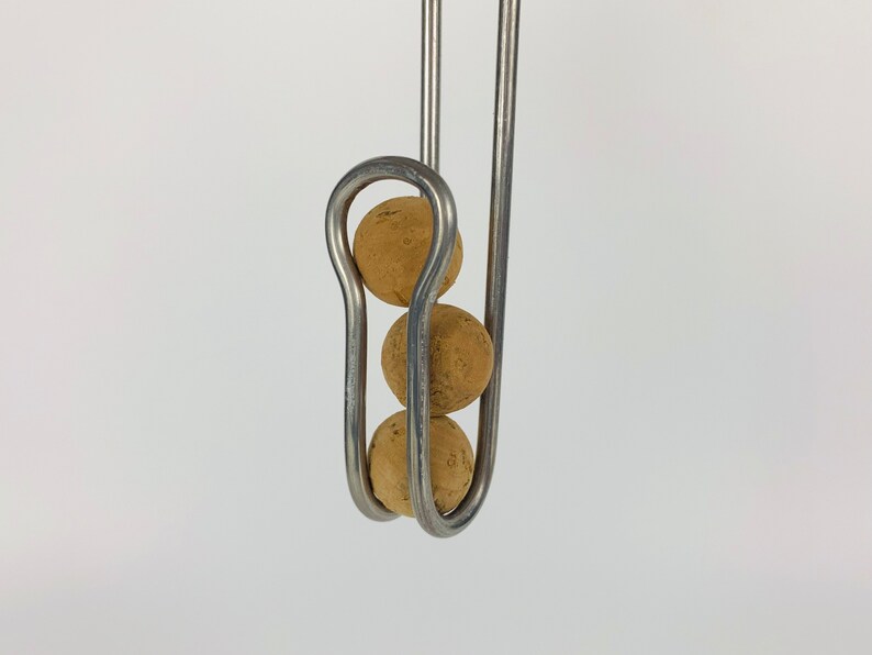 Pu&ograve; includere: Tre sfere di sughero sono sospese da un gancio di metallo. Le sfere sono impilate verticalmente e sono tenute in posizione da un anello di metallo curvo.