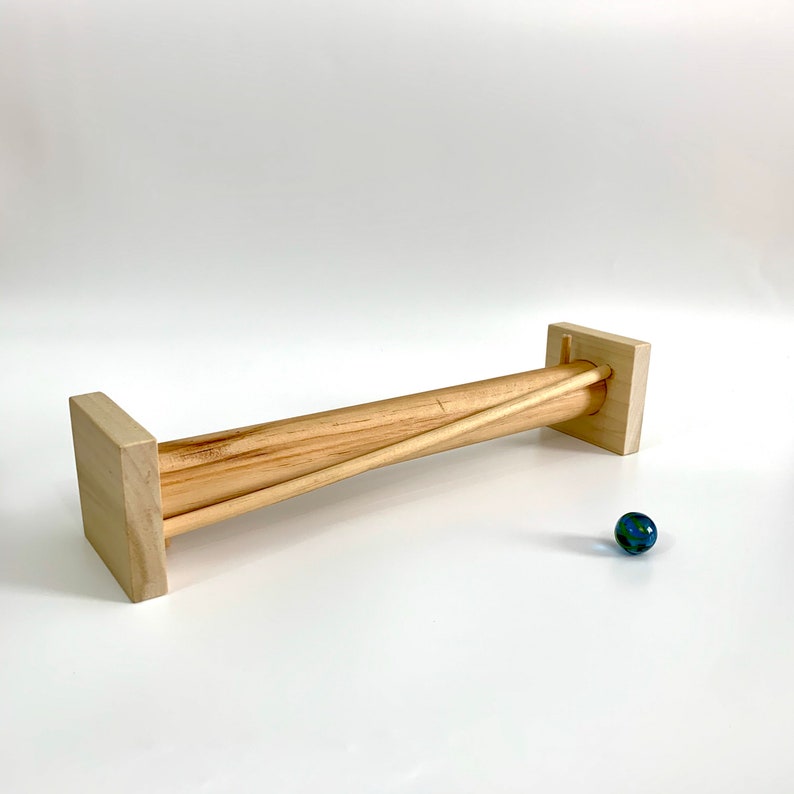 May include: A wooden marble run with two wooden dowels and a blue marble. The marble run is made of natural wood and has a simple design.