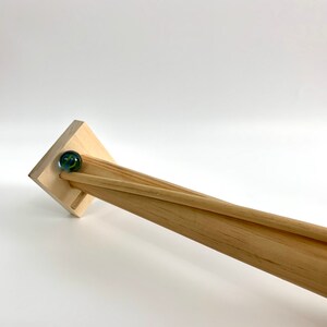 May include: A wooden marble run with a blue and green marble rolling down the track.