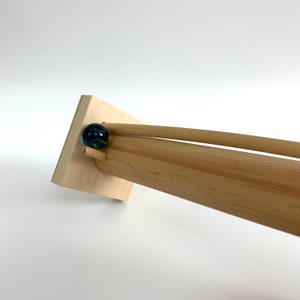 May include: A wooden marble run with a blue and green marble rolling down a track.