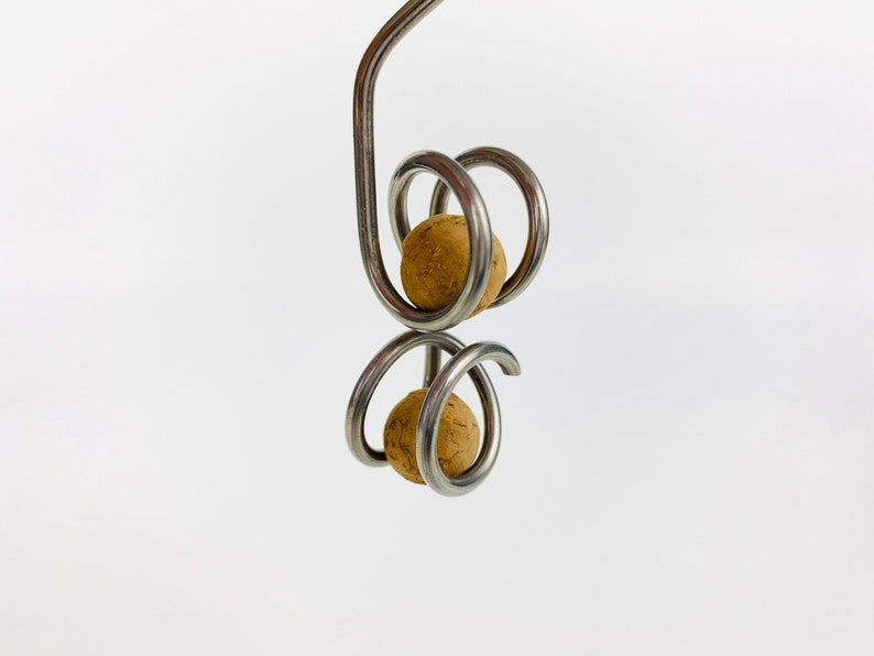 May include: A silver metal wine bottle stopper with two cork balls. The stopper is designed with a spiral shape.