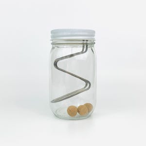 May include: A clear glass jar with a white lid contains three brown balls and a metal wire structure inside.