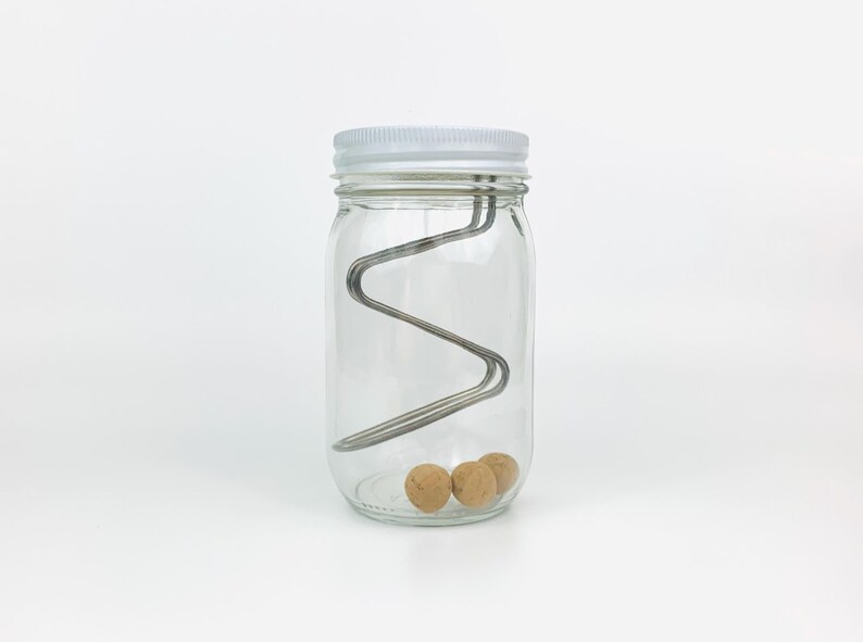 May include: A clear glass jar with a white lid contains three brown balls and a metal wire structure inside.
