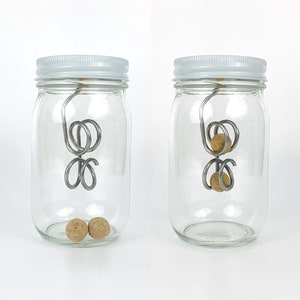 May include: Two glass jars with white lids, each containing a metal wire contraption with cork balls attached. The wire contraption is suspended from the lid of the jar. The cork balls are visible in the bottom of the jar.