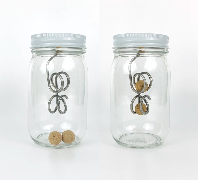 May include: Two glass jars with white lids, each containing a metal wire contraption with cork balls attached. The wire contraption is suspended from the lid of the jar. The cork balls are visible in the bottom of the jar.