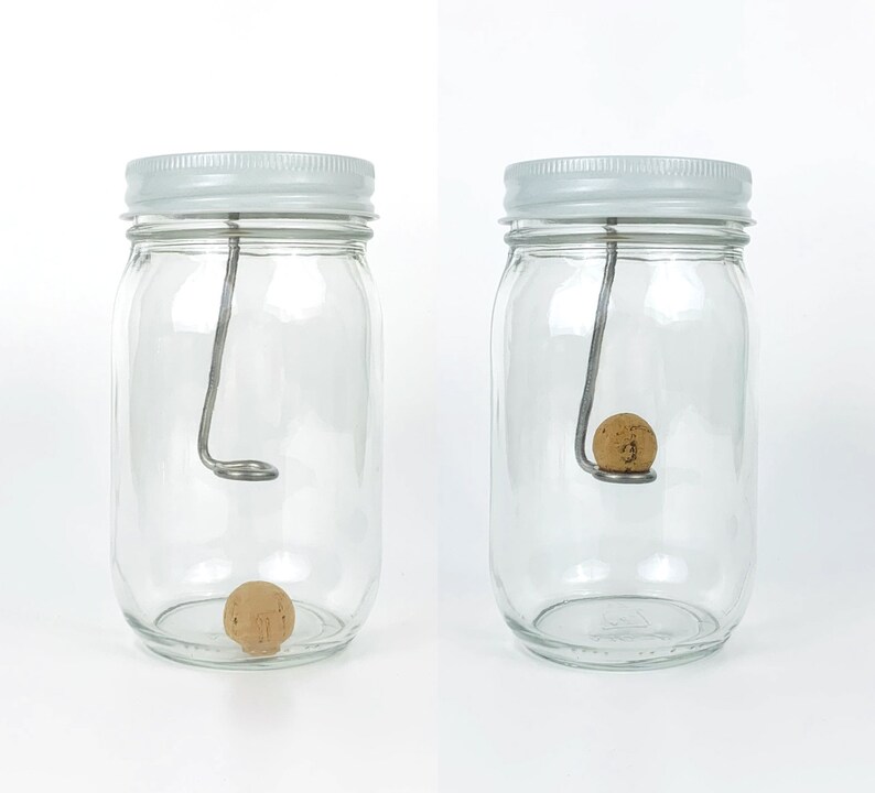 May include: Two clear glass jars with white lids, each containing a cork ball suspended by a metal wire. The wire is bent into a hook shape at the top and is attached to the lid.