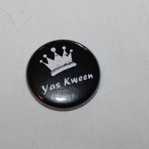 May include: Black and white button with a crown and the text "Yas Kween" printed on it.