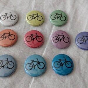 Puede incluir: Una colecci&oacute;n de diez botones redondos con un dise&ntilde;o de bicicleta. Los botones son de varios colores, incluyendo blanco, amarillo, verde, naranja, rojo, morado, azul y turquesa. Cada bot&oacute;n presenta un contorno negro de bicicleta.