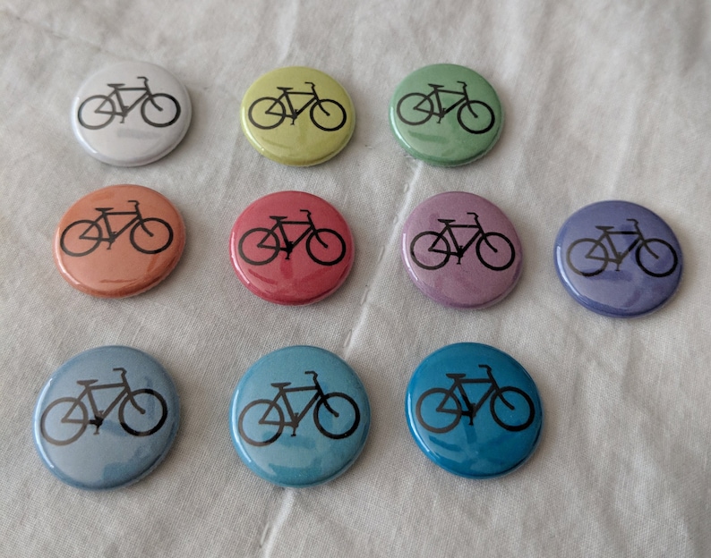 Puede incluir: Una colecci&oacute;n de diez botones redondos con un dise&ntilde;o de bicicleta. Los botones son de varios colores, incluyendo blanco, amarillo, verde, naranja, rojo, morado, azul y turquesa. Cada bot&oacute;n presenta un contorno negro de bicicleta.