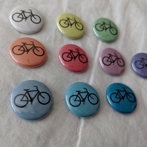 Puede incluir: Una colecci&oacute;n de botones redondos y coloridos con un dise&ntilde;o de bicicleta negra. Los botones est&aacute;n disponibles en varios tonos pastel, incluyendo blanco, amarillo, verde, naranja, rojo, rosa, morado, azul claro y turquesa. Ideales para personalizar ropa o accesorios.