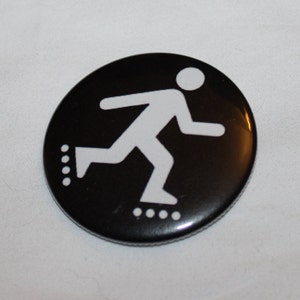 May include: A black and white button with a stick figure rollerblading. The figure is white and the background is black.