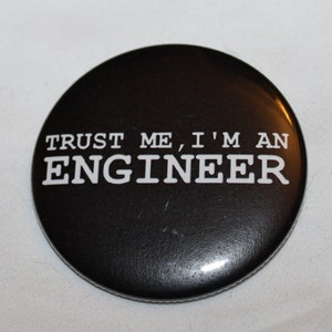 May include: Black and white button with the text "TRUST ME, I'M AN ENGINEER" in white letters.