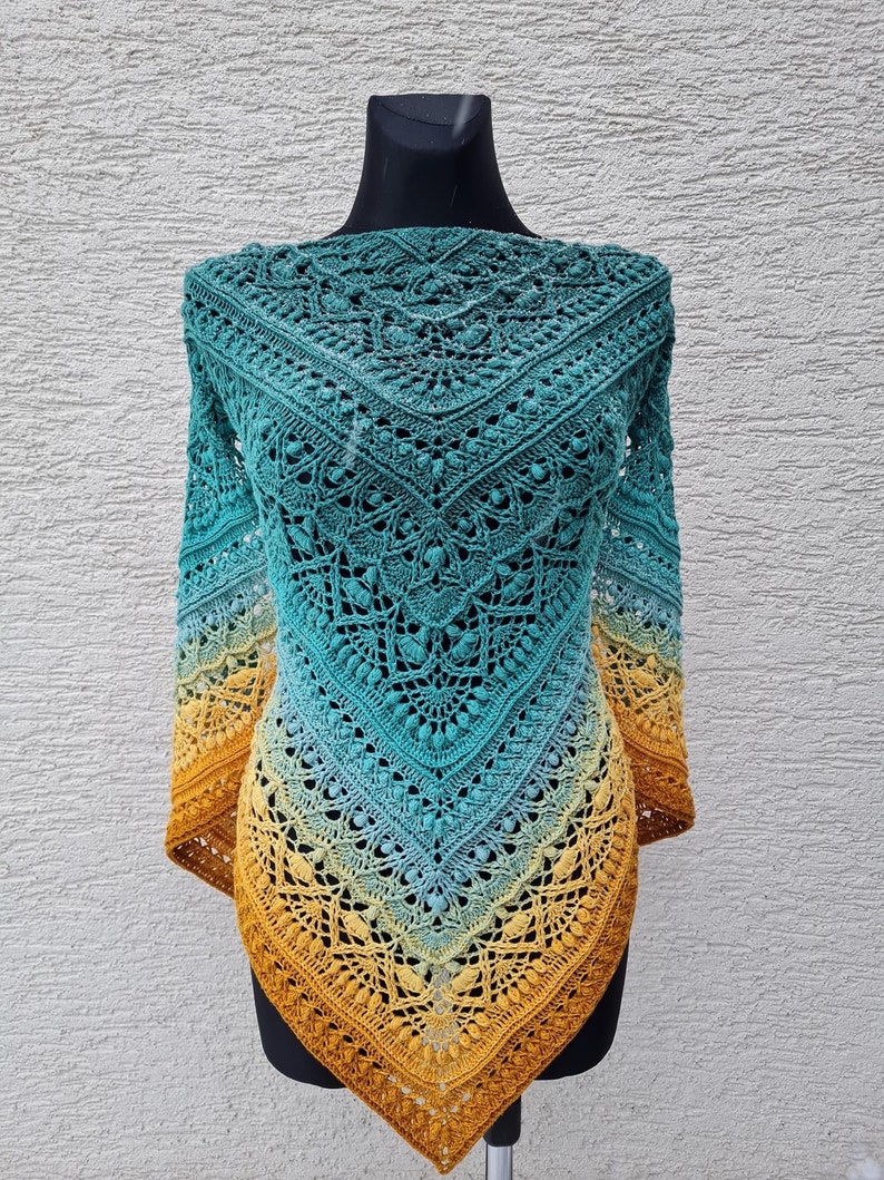 May include: A crocheted shawl with a gradient of teal, blue, and yellow colors. The shawl is made with a delicate lace pattern and has a fringed edge.