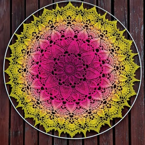 Puede incluir: Un gran doily circular de ganchillo con un dise&ntilde;o degradado de rosa y amarillo. El doily est&aacute; hecho con puntadas delicadas e intrincadas y tiene un borde festoneado.