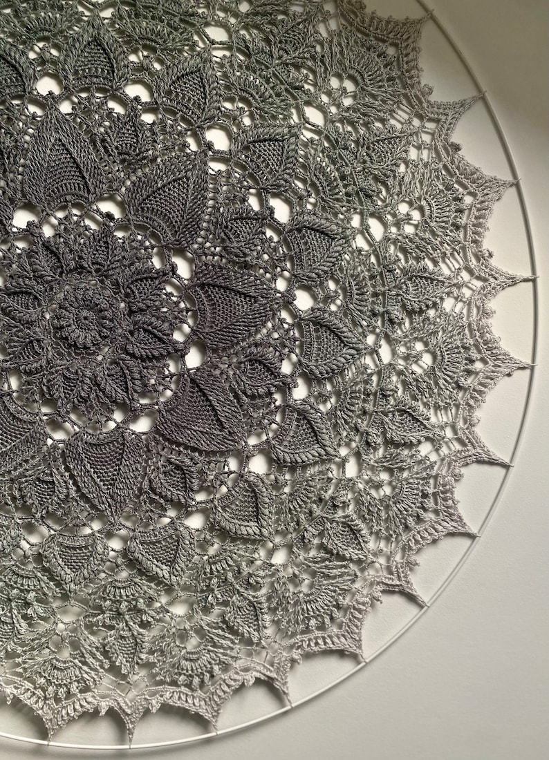 Puede incluir: Un gran encaje de ganchillo circular con un degradado de gris y blanco. El encaje est&aacute; hecho con puntadas delicadas y tiene un dise&ntilde;o intrincado.