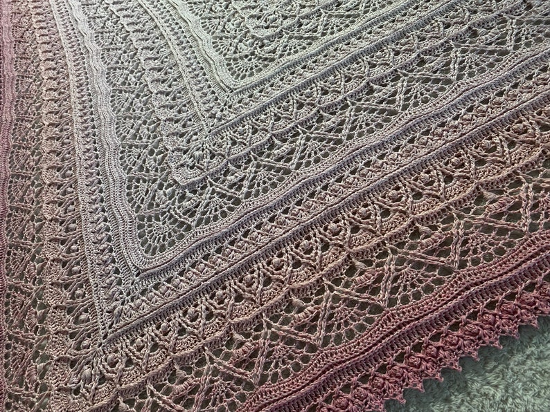 May include: A crocheted shawl with a gradient of pink and gray colors. The shawl has a delicate lace pattern and a scalloped edge.