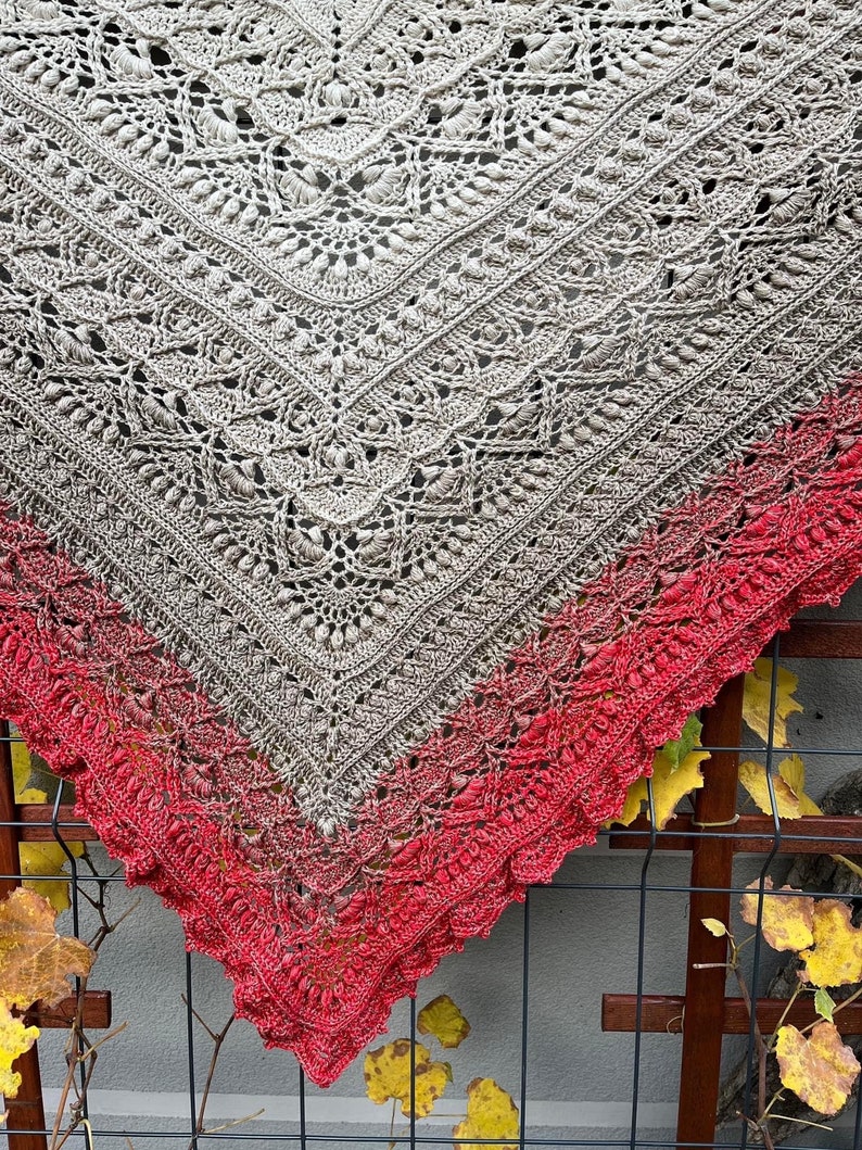 May include: A crocheted shawl with a gradient of colors from beige to red. The shawl is made with a delicate lace pattern and has a scalloped edge.