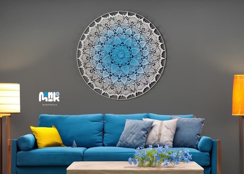 Puede incluir: Un gran tapiz de pared de macram&eacute; blanco con un efecto degradado azul. El mandala est&aacute; colgado en una pared gris sobre un sof&aacute; azul con almohadas. El sof&aacute; est&aacute; en un ambiente de sala de estar con una mesa de caf&eacute; y plantas.
