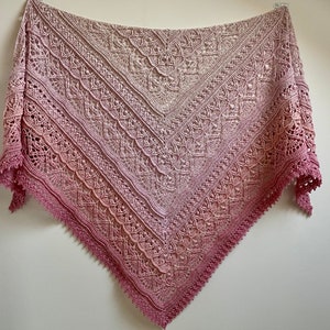 May include: A delicate crocheted shawl with a gradient of pink and beige colors. The shawl has a lacy pattern and a scalloped edge.