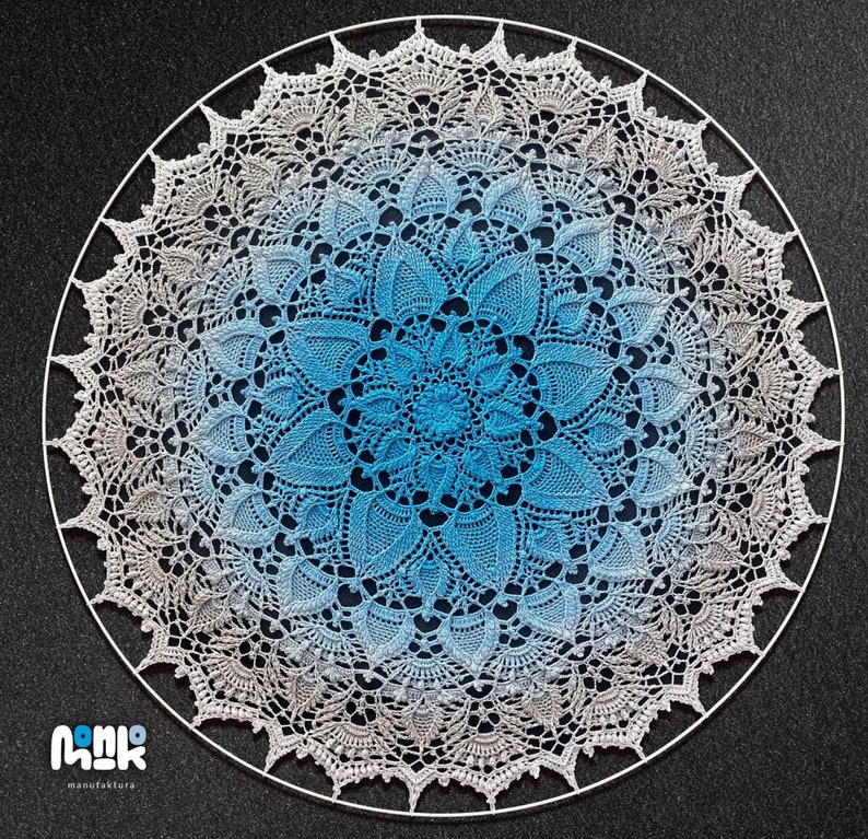 Puede incluir: Un gran doily circular de ganchillo con un degradado de colores azul y blanco. El doily est&aacute; hecho con puntadas delicadas y tiene un dise&ntilde;o intrincado. Se muestra sobre un fondo gris oscuro.