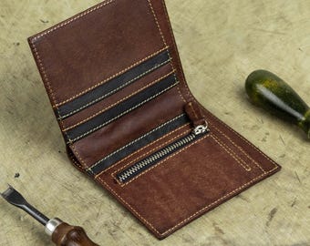 Könnte beinhalten: Offene braune Lederbrieftasche mit Reißverschluss und mehreren Kartenfächern. Die Brieftasche hat schwarze und weiße Nähte und wird mit zwei Lederwerkzeugen gezeigt.
