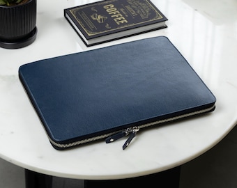 May include: A rectangular navy blue laptop sleeve with a textured surface and a silver-toned metal zip closure featuring two matching navy blue pull tabs. The sleeve is positioned flat, showcasing its clean, structured design and durable construction.
