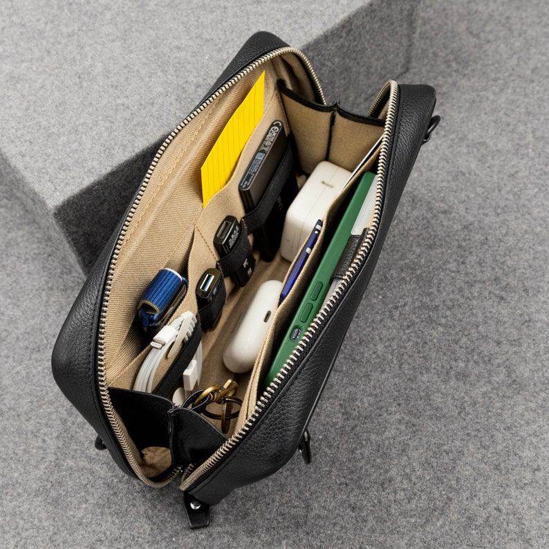 The interior of the leather zippered pouch unzips to reveal a spacious interior with dedicated compartments for your tech gear. Compartments on the left side can carry your pocket notebooks, and cables, USB drives and EDC tools. Compartments on the right are designed to carry a Phone. There is also a pen holder for the Apple Pencil. The section between the two compartments can store bulkier items like the MacBook charger or Air Pods