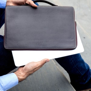 Könnte beinhalten: Eine Person hält eine braune Ledertasche für Laptops mit einem silbernen Laptop darin.