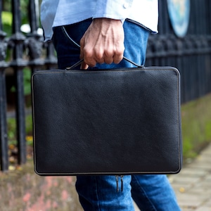 May include: A black leather laptop sleeve with a zipper closure and a brown stitch detail.