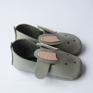 May include: A pair of green leather baby shoes with pink bunny ears. The shoes have a soft, flexible sole and are perfect for little feet.